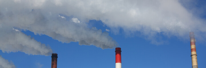 Three pipes of thermal power plant with steam and smoke against blue sky during heating season. Work CHP concept