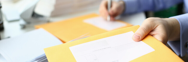 Secretary fills in address on yellow postal envelope for sending letters. Business correspondence...