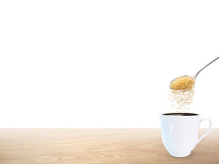 A spoonful of granulated sugar is poured into a white coffee mug placed on a wooden floor.