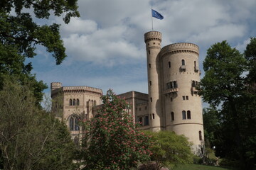 Yellow brick castle with round towers through the green trees