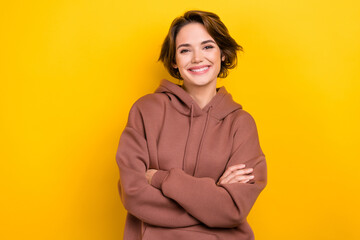 Photo portrait of confident cheerful lady hold crossed arms good mood wear brown hood shirt isolated yellow color background
