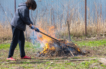 A young woman in a black jacket burns dry grass in the yard
