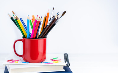 Bright pencils in a red mug on the books on the desk. Back to school. Banner. Place for text. Selective focus.