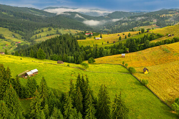 Obraz premium Travel to Bucovina, Romania. Aerial view over a farm with haystacks in a beautiful village mountain area from Suceava.