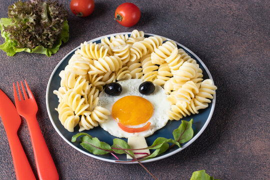 Fun Food for kids - smiling face from fried eggs, pasta fusille, olives and leaves beets on blue plate