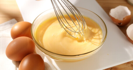 Whisking eggs. Whipped raw eggs in a bowl with whisk. Breakfast preparation. Rustic style. Sunny day. Smooth camera movement. Close up. 4k footage.