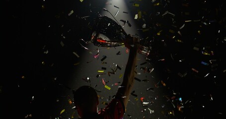 Silhouette of Caucasian male soccer football player raising a trophy above head against bright...