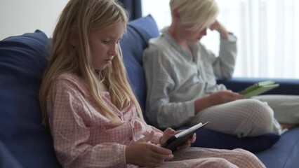 Brother and sister, a girl and a boy, play on a tablet in the morning