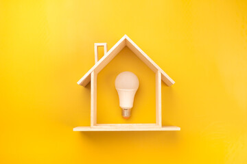 White light bulb in model wooden house on bright yellow background. Energy saving light bulb on...