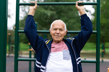 Fototapeta na wymiar Active grandpa pulls up on horizontal bar on sports ground