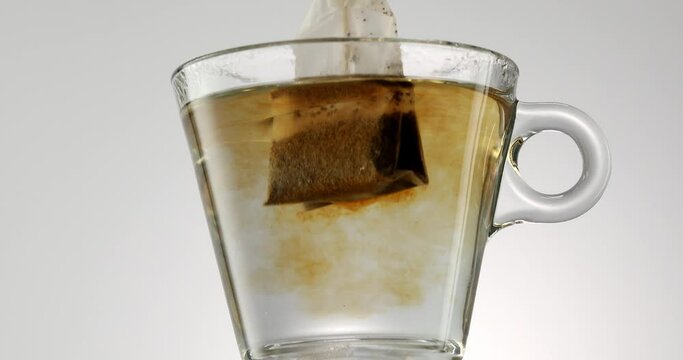 Brewing tea with a tea bag. A transparent mug on the table with boiling water, the tea bag dissolves. The water slowly turns cinnamon-colored. Cozy morning, making tea. 4k footage.