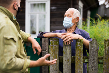 Good neighbors in protective mask talk on border of their farms