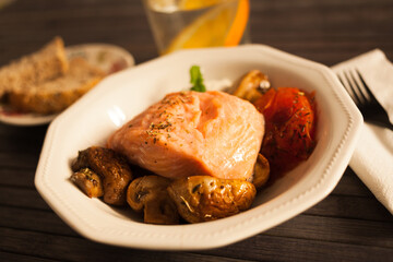 steamed sea trout fillet served on fried mushrooms with tomatoes in a white bowl