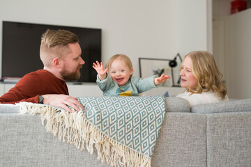 Parents playing with smiling baby Parents with baby with down syndrome reading a book on sofa on sofa in living room