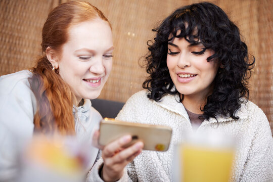 Young women using phone and laughing at meme in cafe