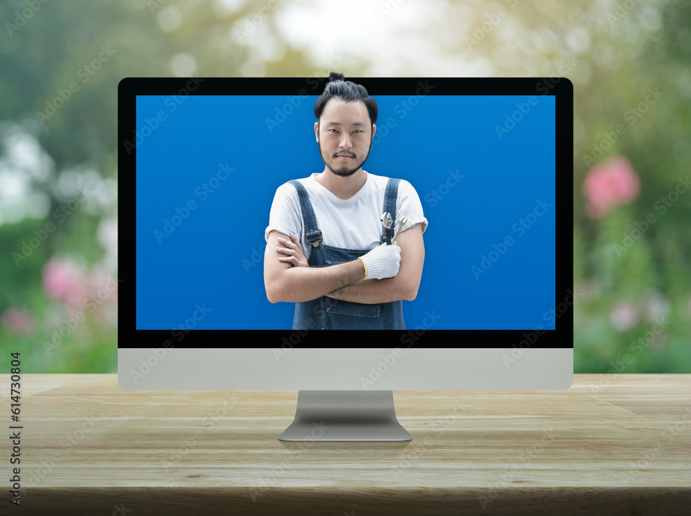 Poster asian mechanic car engine in uniform with tools on modern computer monitor screen on wooden table ov