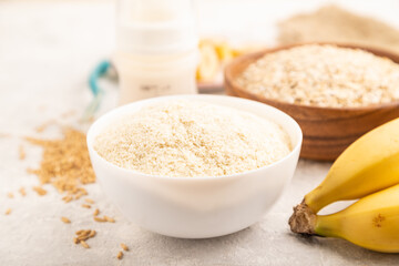 Powdered milk and oatmeal, banana baby food mix, on gray concrete, side view, selective focus