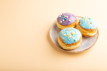 Purple and blue glazed donut on orange pastel, side view, copy space.