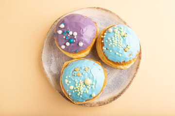 Purple and blue glazed donut on orange pastel, top view.
