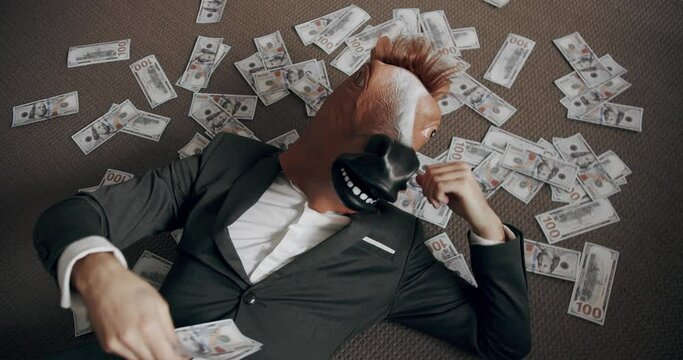 Funny man with horse mask in a suit enjoying his financial success and counting money sitting down on the floor. Man with horse mask throw money. Money rain, falling dollars.