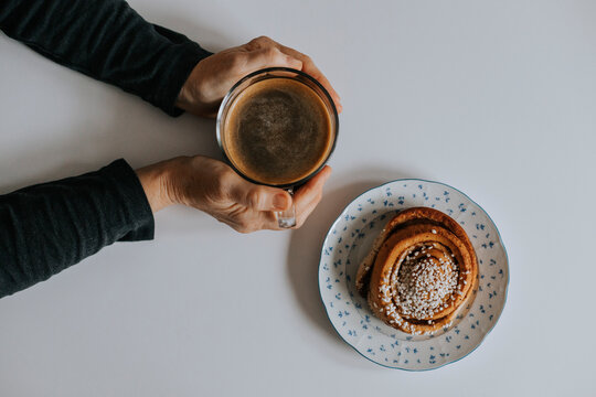 Hands holding coffee cup with cinnamon roll on table