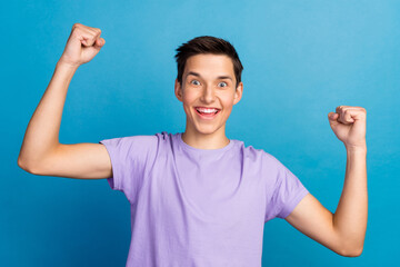 Portrait of very excited young man celebrating victory with raised hands and screaming isolated blue color background