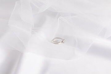 Two white gold wedding rings lie on a white classic bridal veil and a satin fabric background. The concept of the wedding. cover, invitation.