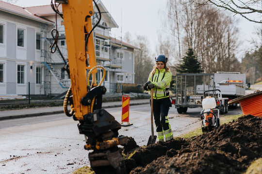 Female road worker and excavator at digging site