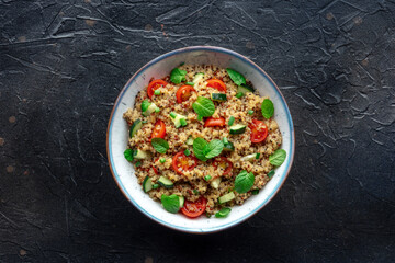 Quinoa tabbouleh salad in a bowl, a healthy dinner with tomatoes and mint, overhead shot on a black slate background