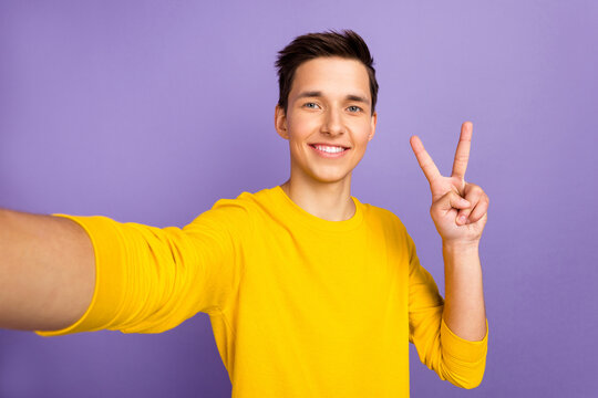 Photo of young cheerful man make v sign take selfie influencer journey isolated over shine color background