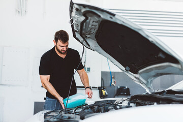 Car mechanic filling up windshield washer fluid in workshop