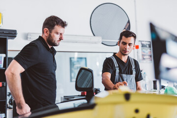 Car mechanics working to remove dent in workshop.