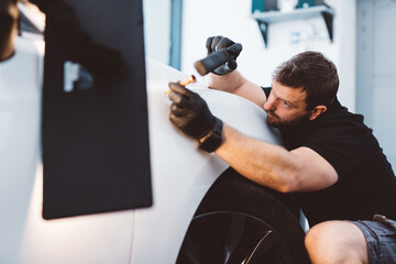 Car mechanic working to remove dent in workshop.