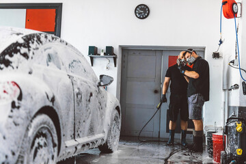 Service man washing car before detailing in workshop.