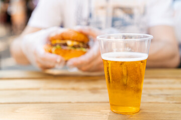 Glass with iced beer and man eating burger on background