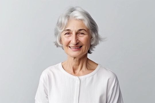 Beautiful 60s mid aged mature woman looking at camera. Mature old lady close up portrait on a grey background