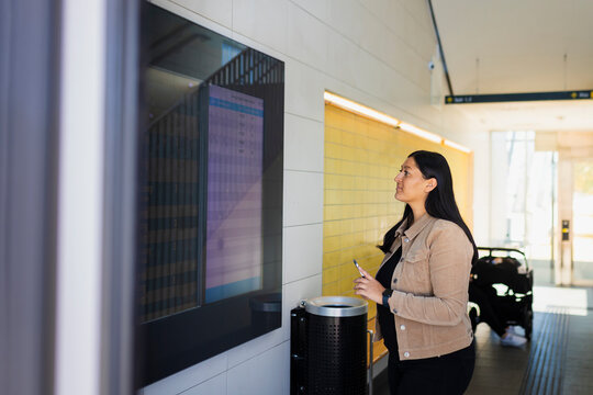 Woman at railway station looking at arrival and departure board on screen