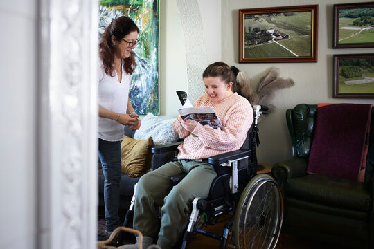 Mother with disabled daughter in wheelchair in living room, teenage girl reading magazine