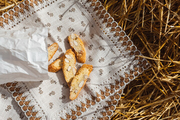 Almond cookies crackers with pieces of nuts fell out of a paper bag on a napkin lying on the straw,...