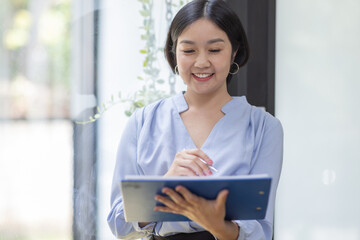 Boring young business Asian woman holding document file and looking at camera stand on a workplace office.