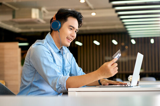 Asian casual businessman smile and present a credit card on  conference meeting with laptop in co-working space