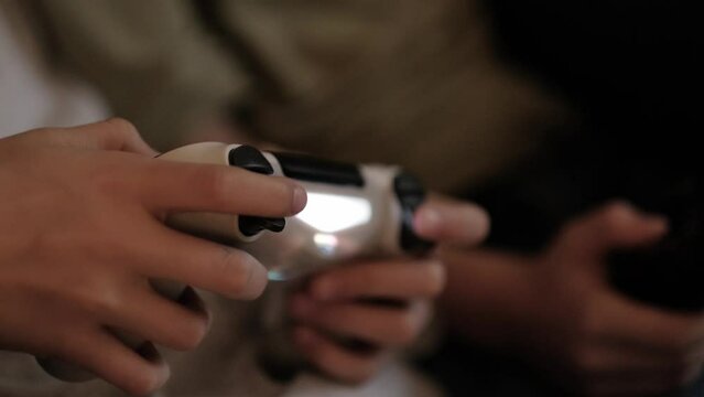 kids hands with joysticks, two children siblings playing video game console while sitting at home, real people, leisure concept.
