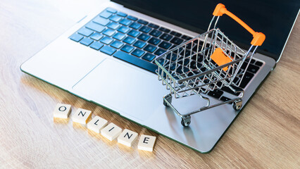 Online shopping concept. Shopping cart or trolley and laptop on wooden table.