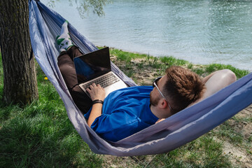 Man in Hammock with Laptop by River. Relaxing work environment