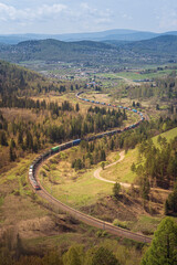 A winding railway among forests, mountains and hills. Cargo delivery beautiful vertical photo