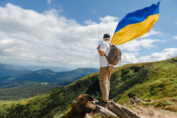 A tourist on the mountains with a ukrainian flag - obrazy, fototapety, plakaty