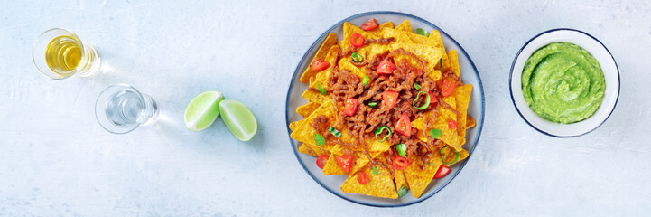 Nachos panorama, Mexican food, tortilla chips with beef and fresh vegetables, overhead flat lay shot with tequila, limes, and guacamole