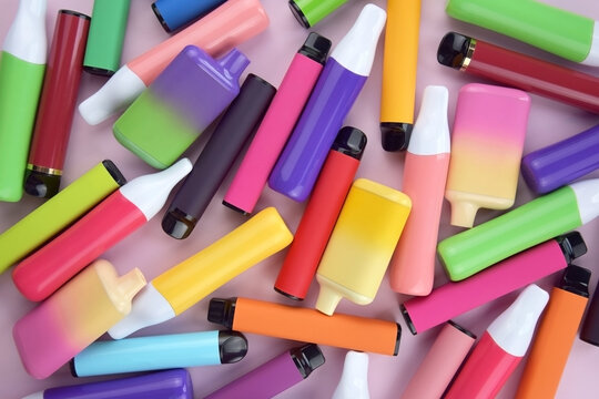 Set of multicolor disposable electronic cigarettes on a pink background.