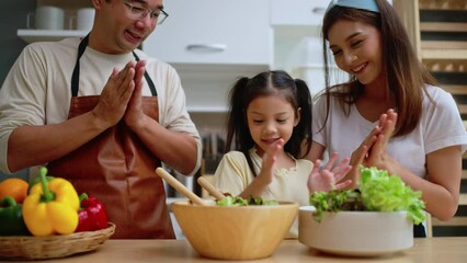 Young asian family cooking food in kitchen.Cute little girl and her beautiful parents are making salad and smiling while cooking in kitchen at home.Happy family in the kitchen concept.