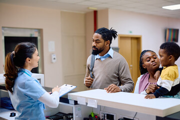 Black parents with small son talk to reception nurse at doctor's office.